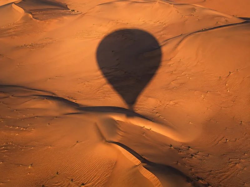 Balloon shadow stretching across the dunes below the basket