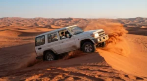 White Land Cruiser 4x4 with passengers climbing a red-orange sand dune as sand sprays from its wheels