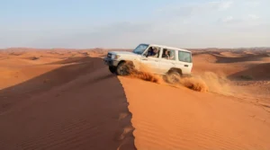 White Land Cruiser 4x4 with passengers driving along a red sand dune crest near Dubai in clear morning light