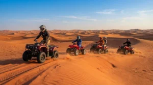 Five helmeted riders on red quad bikes, one carrying a passenger, cross red dunes near Dubai in warm light